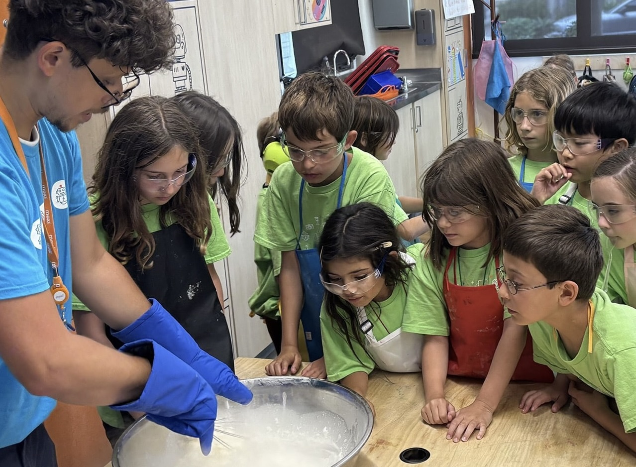 A group of children eagerly watchning an instructor prepare prepare a large bowl of plaster for a display.